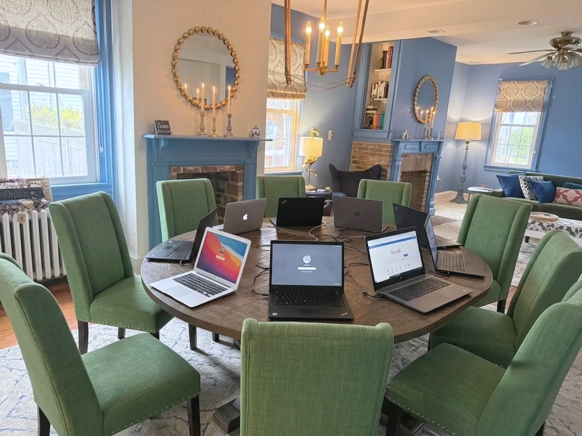 Eight green chairs and eight open laptops arranged around a dining table in Emily’s home.